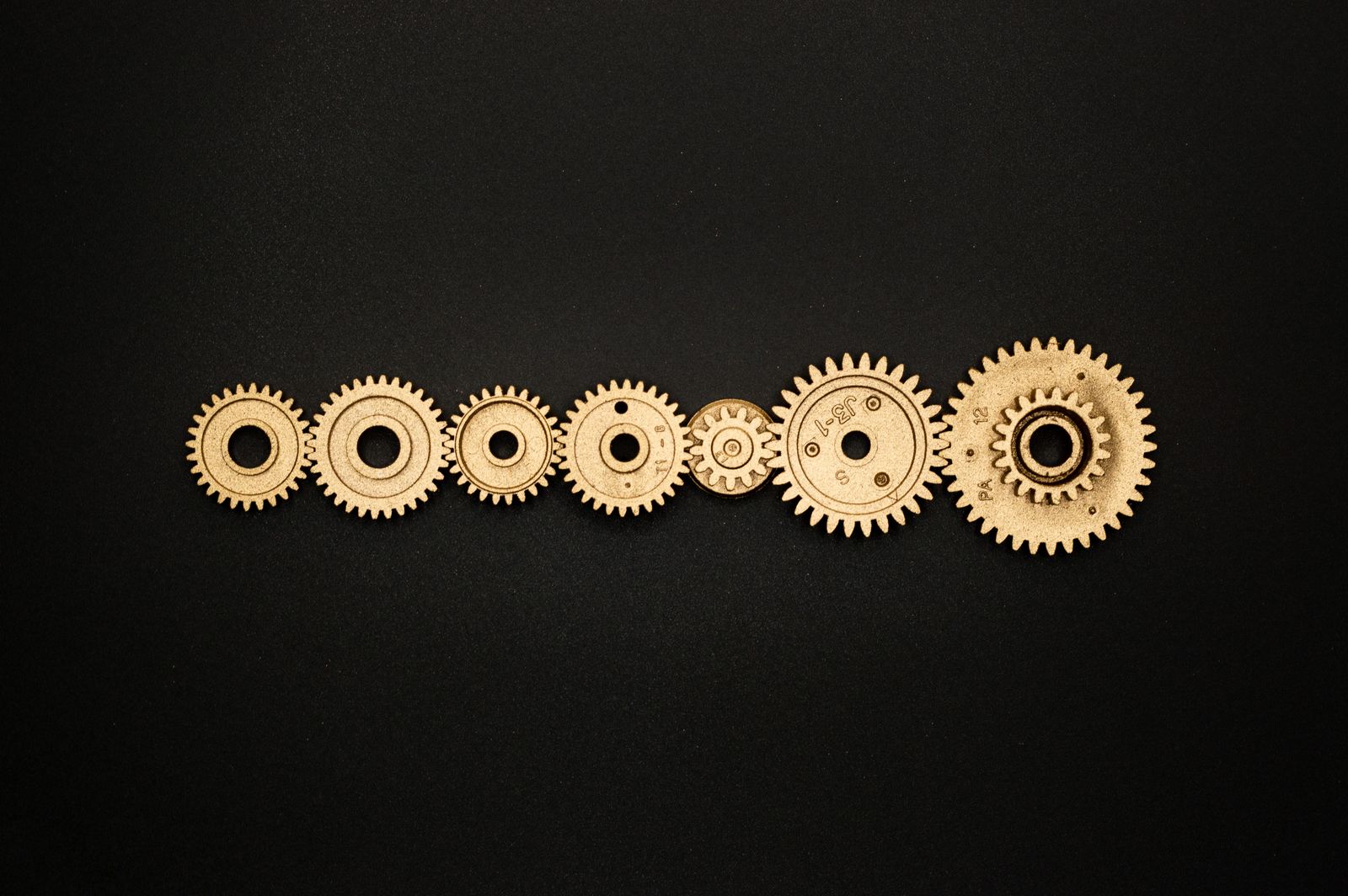 A row of gilded gears on a black background — from small to large, like estimate classes